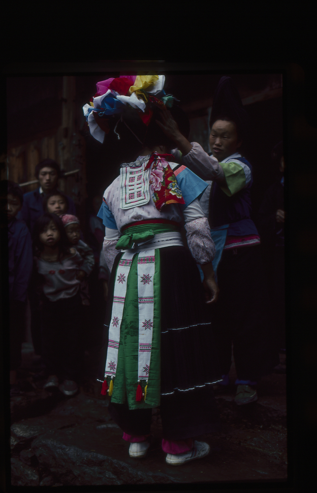 Image of 35mm slide: A girl having her head dress put on.