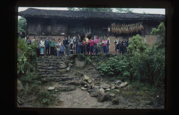 Image of 35mm slide: Saturday 29th Farewell line-up outside a house. Rice hanging from the eaves.