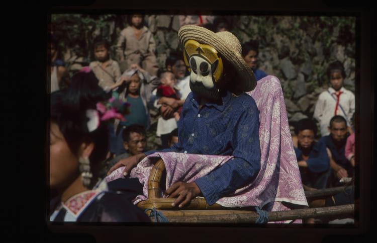 Image of 35mm slide: Masked man in carrying chair