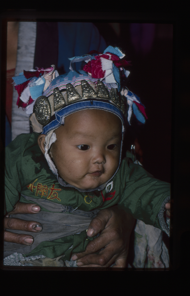 Image of 35mm slide: Baby with headdress (similar row of amulets in collections)