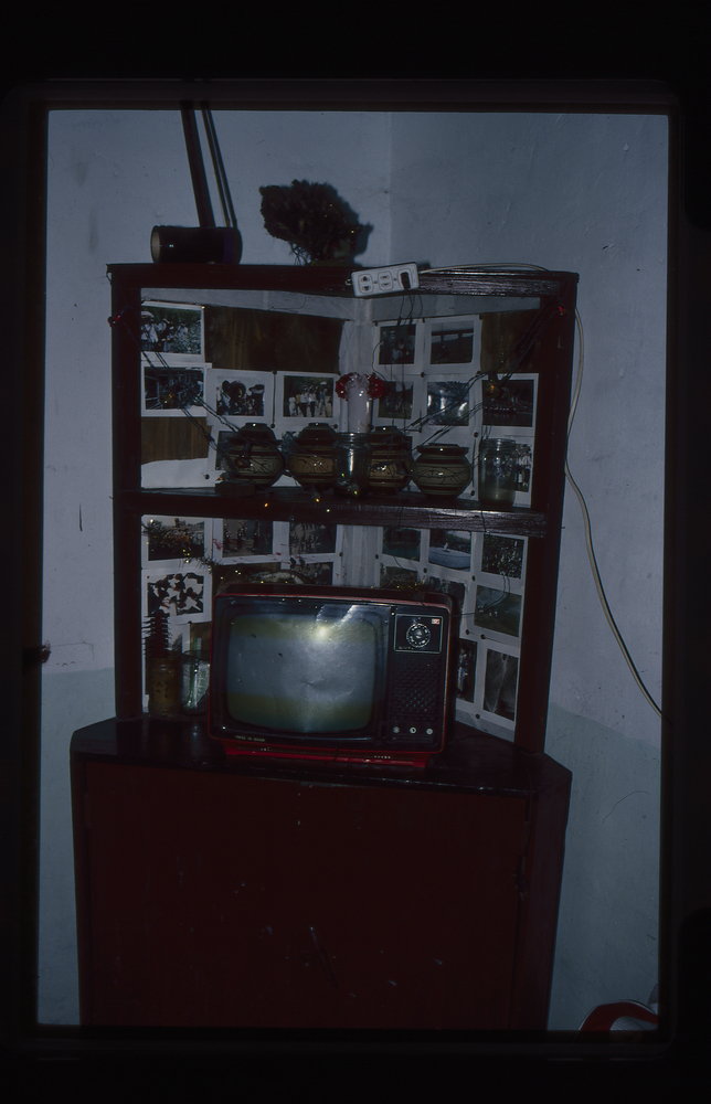 Image of 35mm slide: Personal photographs and television inside house of well-to-do villager