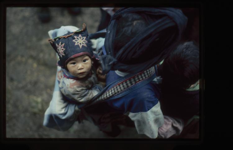 Image of 35mm slide: Child with head dress in baby carrier