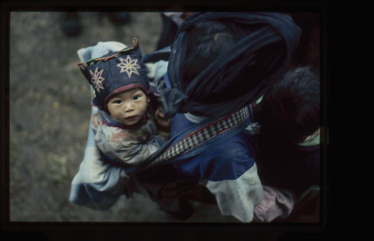 Image of 35mm slide: Child with head dress in baby carrier