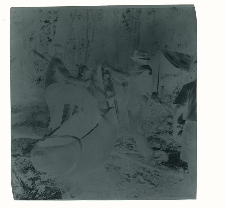 Image of Black and white negative of men building canoe on dry land next to tents