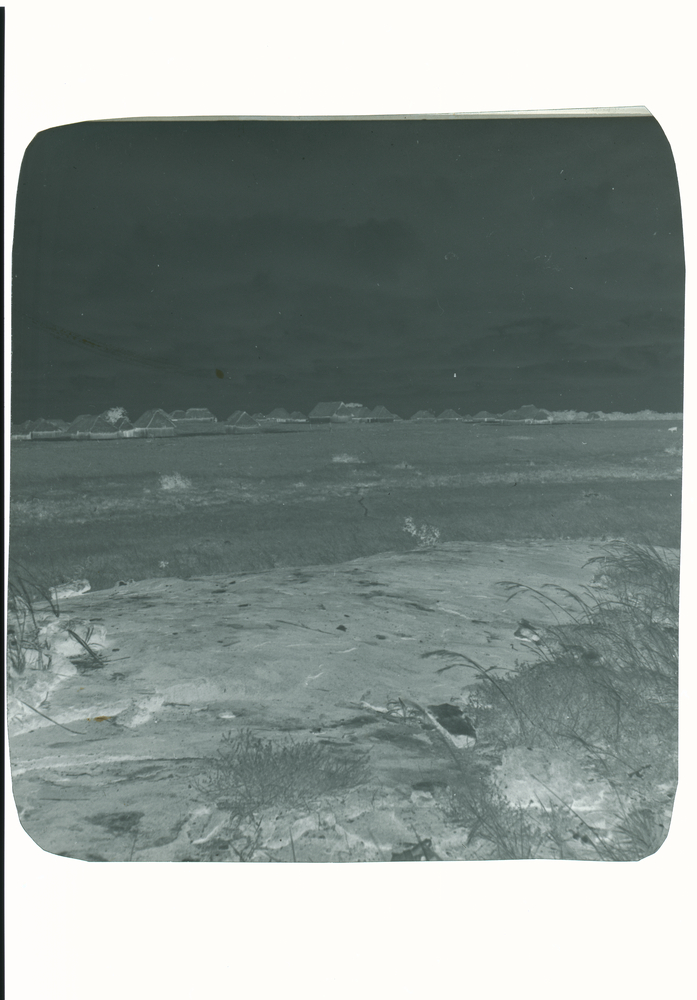 Image of Black and white negative of rocky open field with multiple huts in distance