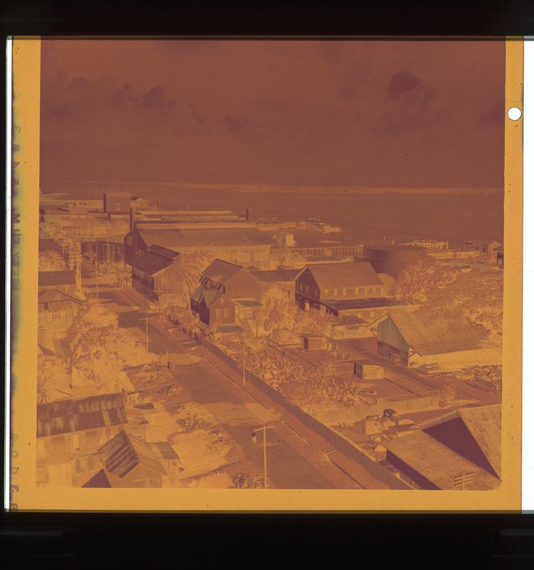 Image of Orange (sepia?)-toned negative view of street with buildings on coastline in tropical climate setting