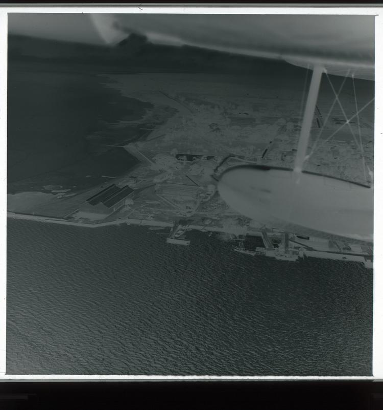 image of Black and white negative view from air of double coastline of industrial-looking part of town with wing in frame and water
