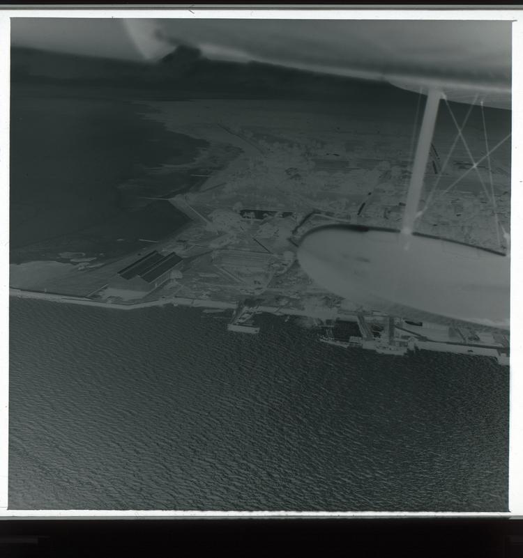 Image of Black and white negative view from air of double coastline of industrial-looking part of town with wing in frame and water