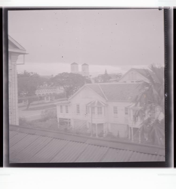 Image of Black and white negative of multiple buildings, closest a building with elevated parts with multiple trees