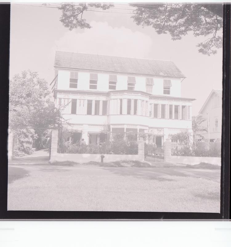 image of Black and white negative front view of building with multiple windows and front yard full of trees