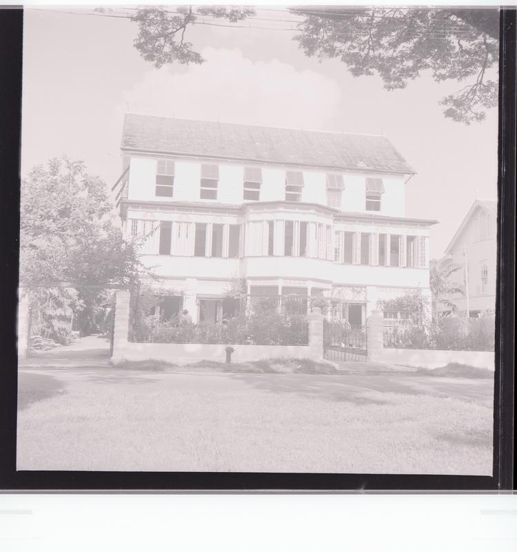 Image of Black and white negative front view of building with multiple windows and front yard full of trees