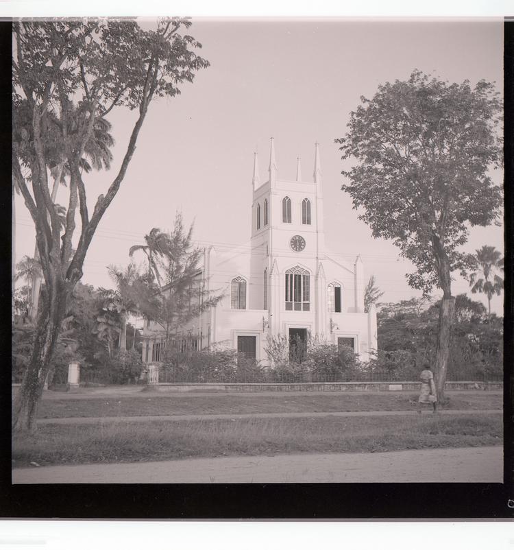 Image of Black and white negative view of ornate church with multiple steeples and trees in front