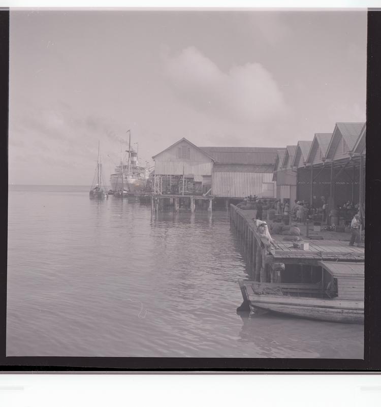 image of Black and white negative of docked ship with people in front of port building