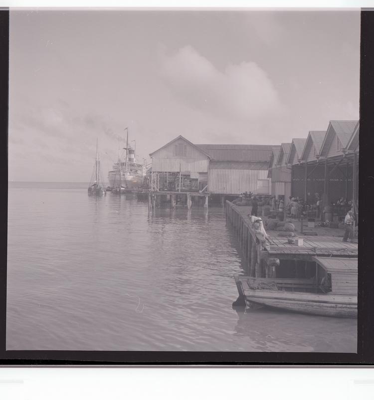 Image of Black and white negative of docked ship with people in front of port building