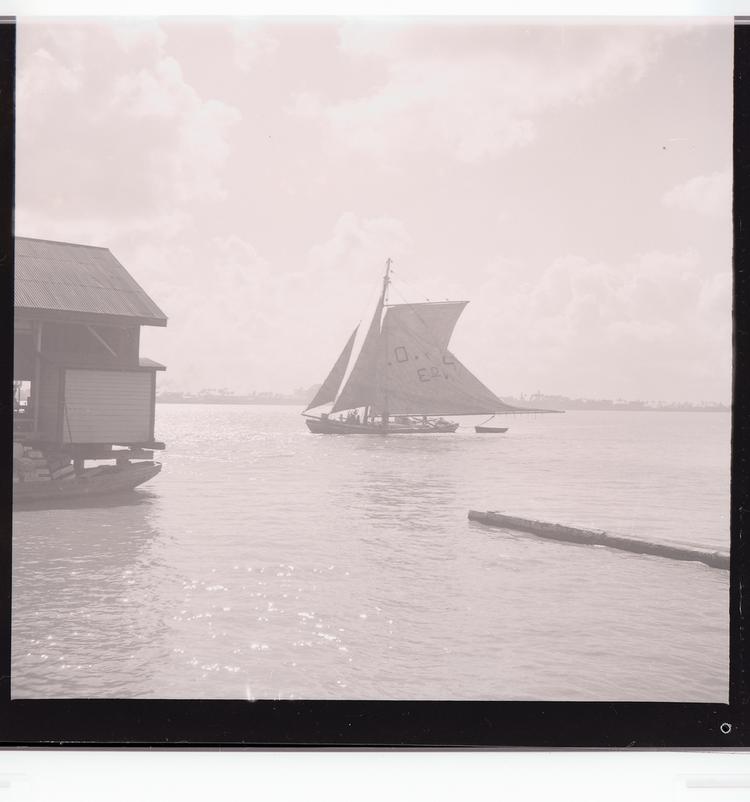 image of Black and white negative of ship sailing into (out of?) port with part of dock in mid-ground