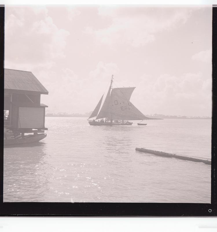 Image of Black and white negative of ship sailing into (out of?) port with part of dock in mid-ground