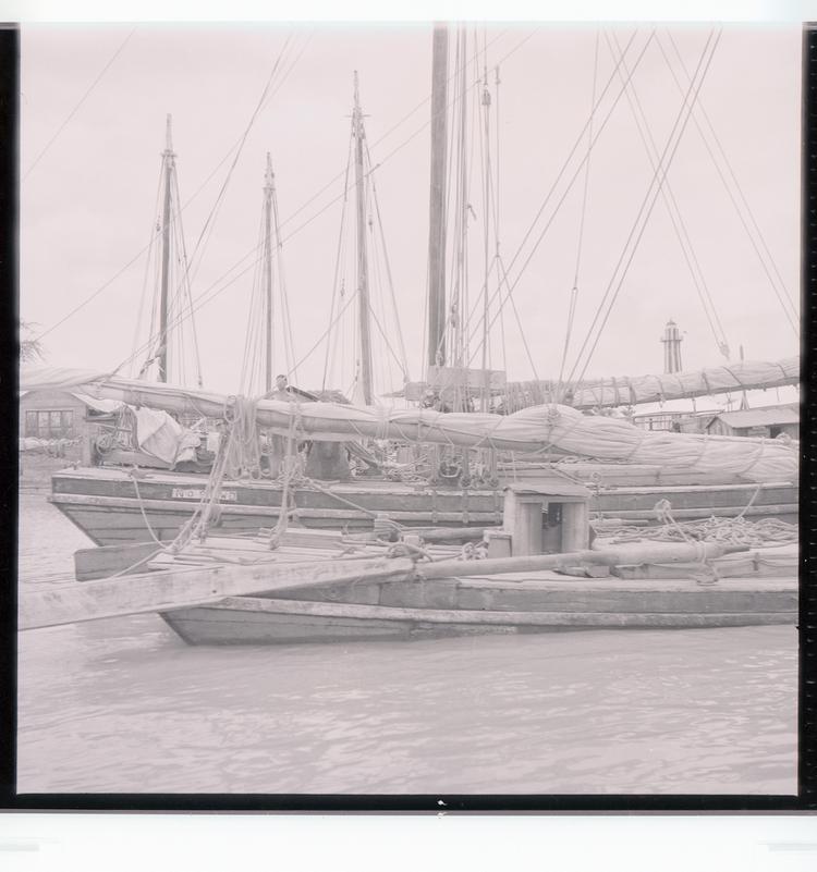 image of Black and white negative of docked boats with high masts and person on boat
