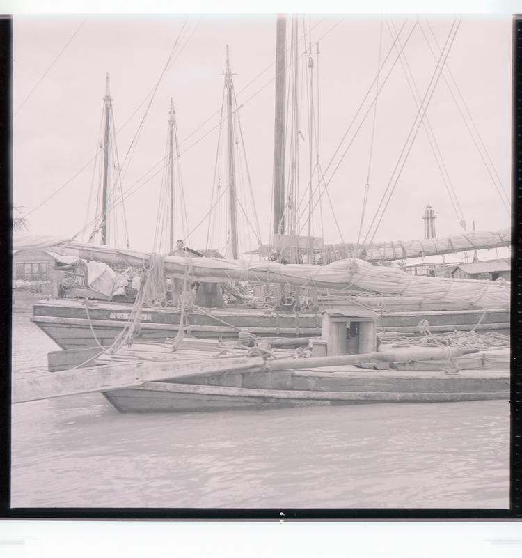 Image of Black and white negative of docked boats with high masts and person on boat