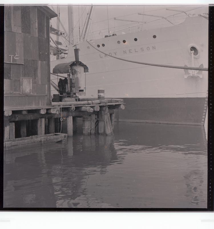 Image of Black and white negative of the Lady Nelson ship docked next to building