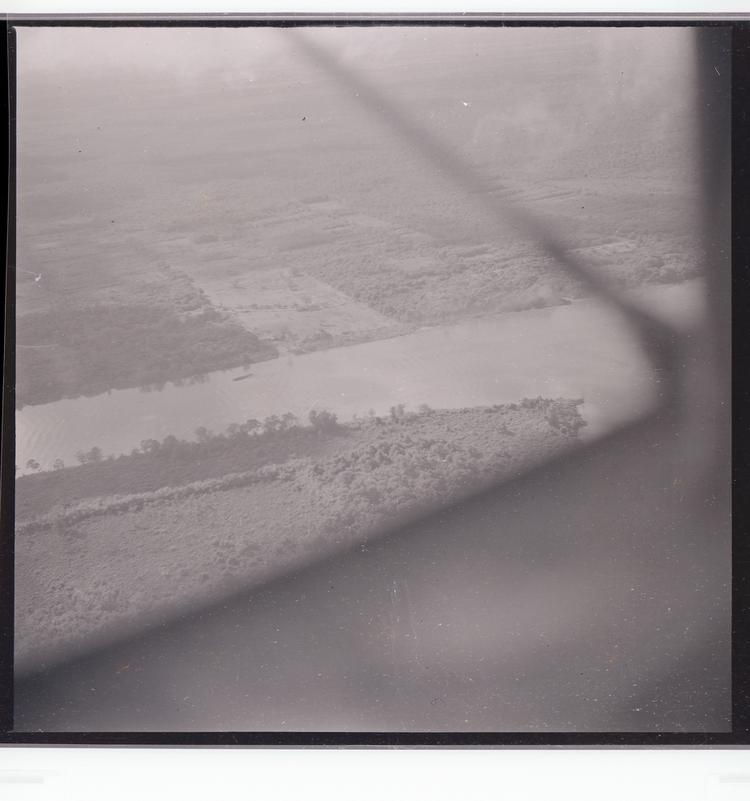 image of Black and white negative of tree-lined canal from air with part of wing/plane obstructing view