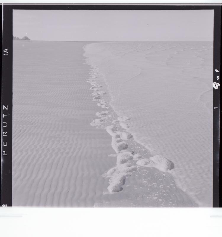 image of Black and white negative of rocks on shoreline where water reaches the beach
