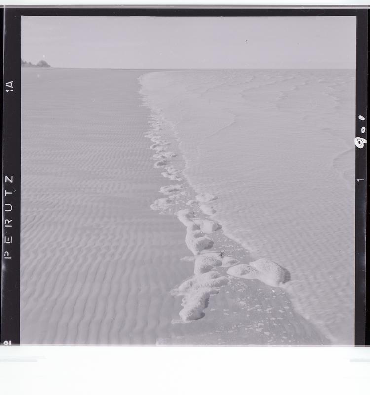 Image of Black and white negative of rocks on shoreline where water reaches the beach