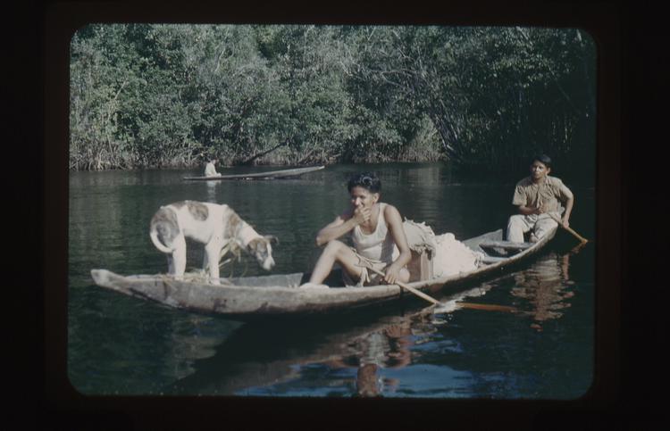 Image of Color 35mm positive film of two men and one dog in a low canoe on a river, with one man in a canoe in background