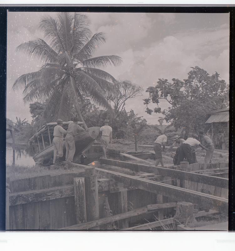 image of Black and white negative of people loading boats on slats