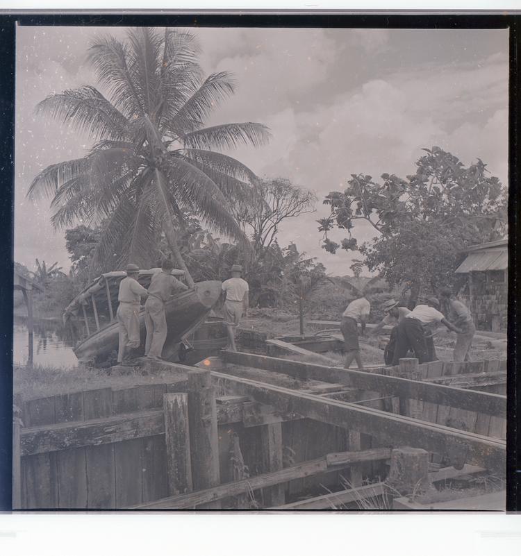 Image of Black and white negative of people loading boats on slats