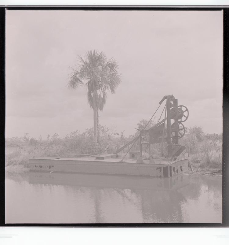 Image of Black and white negative of structure with multiple gears floating in tree-lined canal