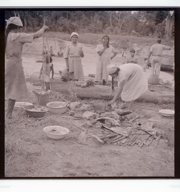 image of Black and white negative of many people (mostly women) tending to dead animals parts on dock