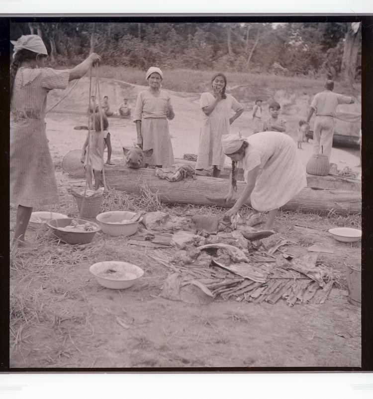 Image of Black and white negative of many people (mostly women) tending to dead animals parts on dock