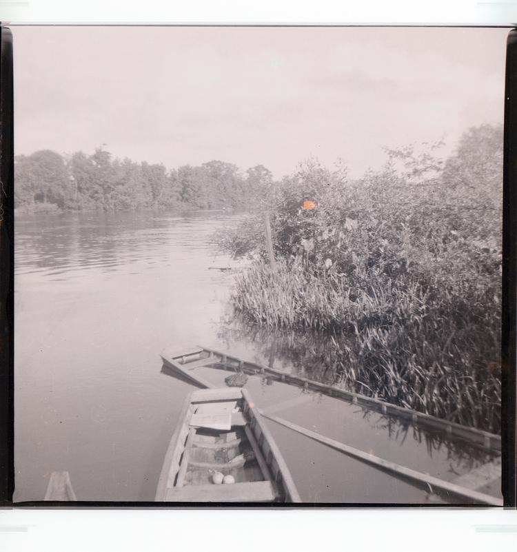 Image of Black and white negative of small boat pulled up in wetland area with other boat half sunk