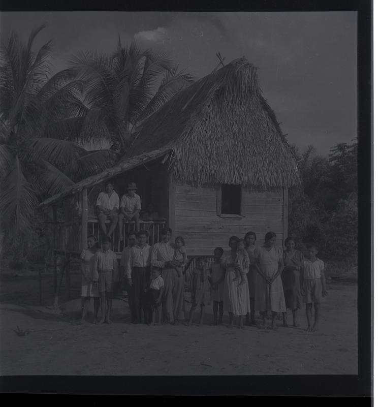 image of Black and white medium format negative (scanned positive) of a large family group in front of a thatched house