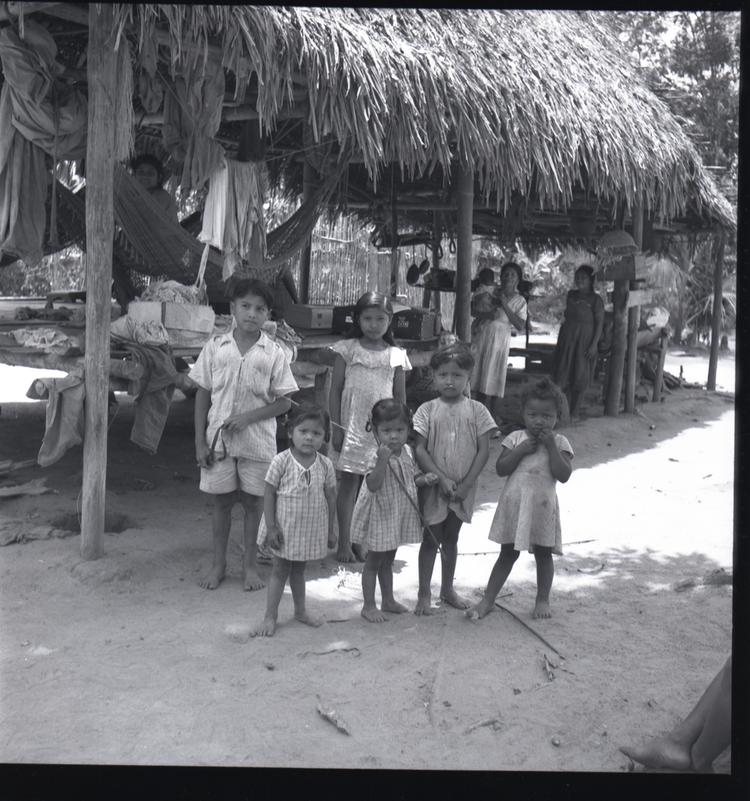 Image of Black and white medium format negative (scanned positive) five children posed in front of thatched house with women and a baby in background