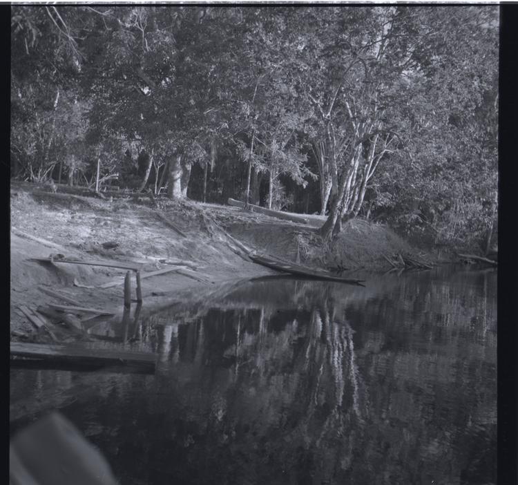 Image of Black and white medium format negative (scanned positive) picturesque river scene with a moored canoe and trees reflected in the water