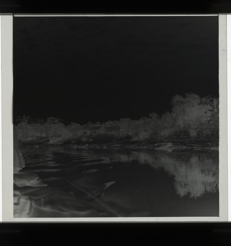 Image of Black and white negative of buildings on tree-covered sand dunes, view from moving boat on river