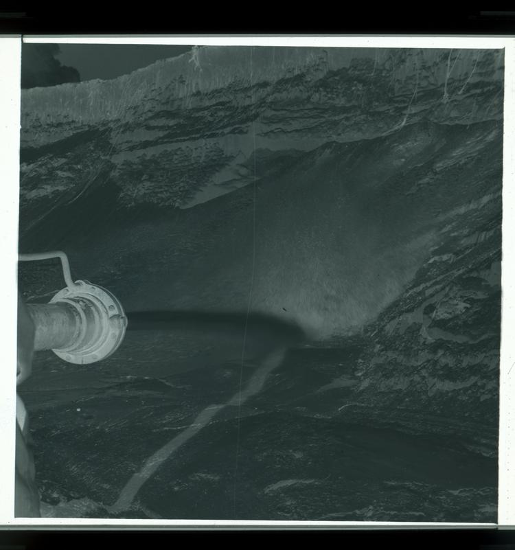image of Black and white negative of hydraulic jet blowing into wet sand, close-up