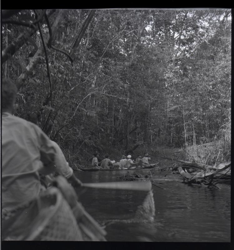 image of Black and white medium format negative (scanned positive) of a wooden canoe with 6 men in it, photo taken from another boat