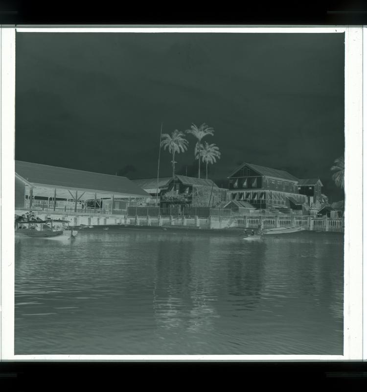 image of Black and white negative of buildings on waterfront and covered dock with boats on either side of frame