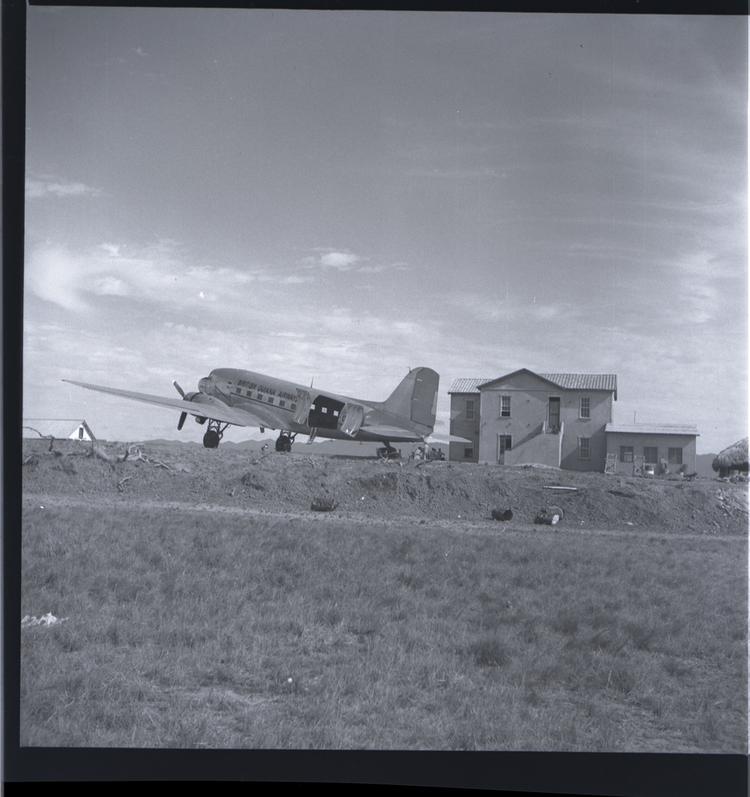 Black and white medium format negative of plane on ground near a building