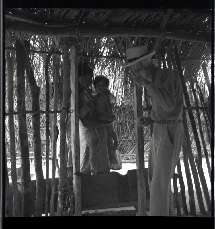 Black and white medium format negative of man talking to a woman holding a child in a wooden hut