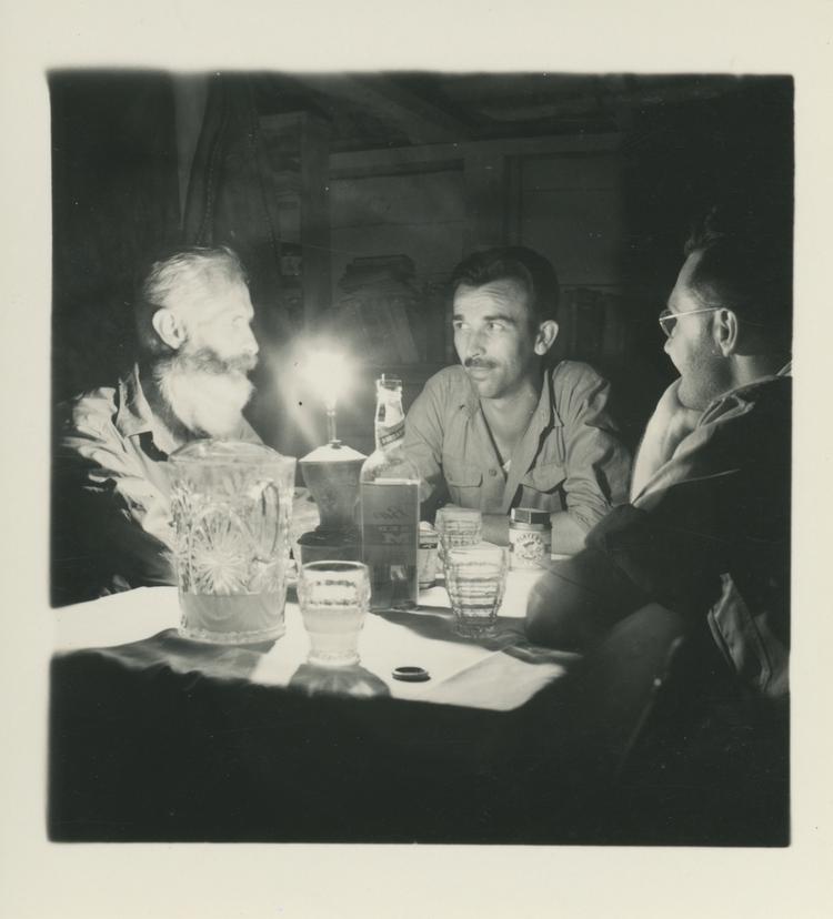 image of Black and white print of 3 men sitting at a lamplit table with drinks