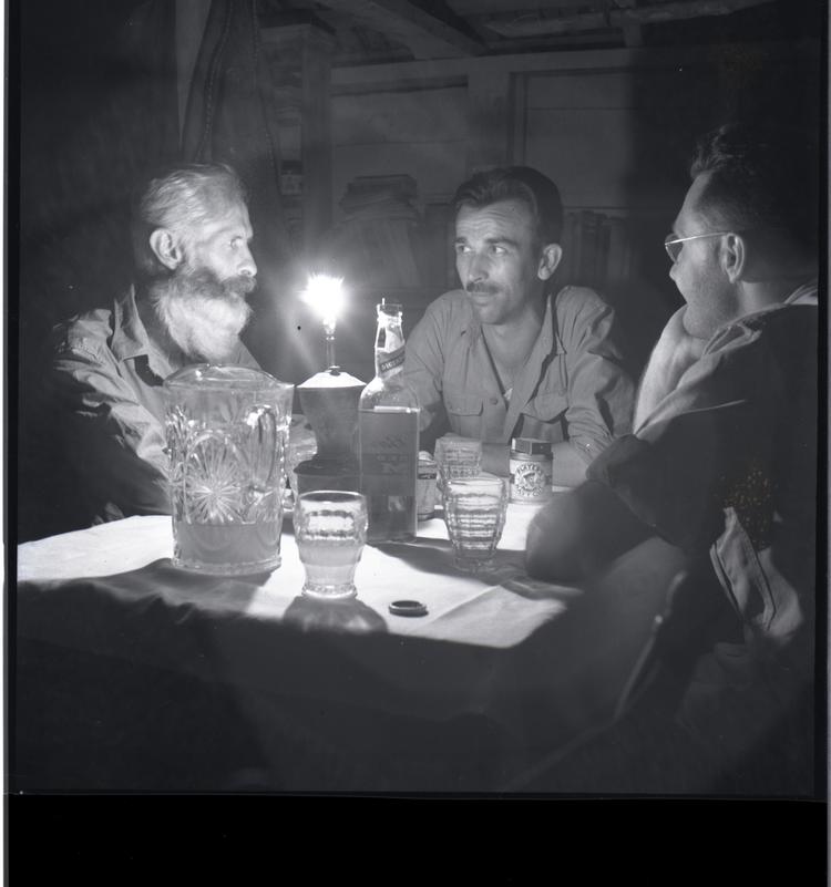 image of Black and white medium format negative of 3 men sitting at a lamplit table with drinks