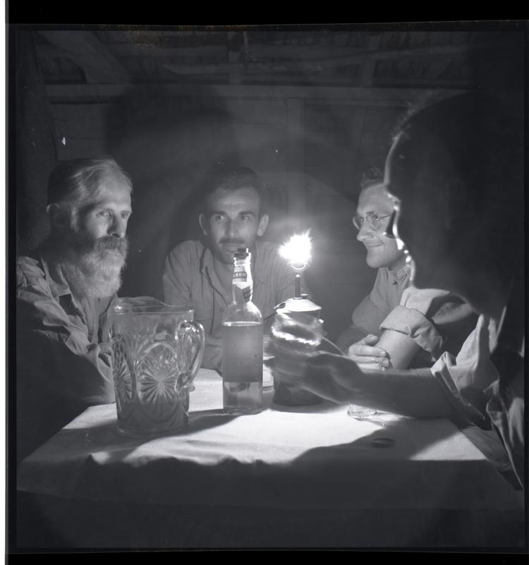 image of Black and white medium format negative of 4 men sitting at a lamplit table with drinks