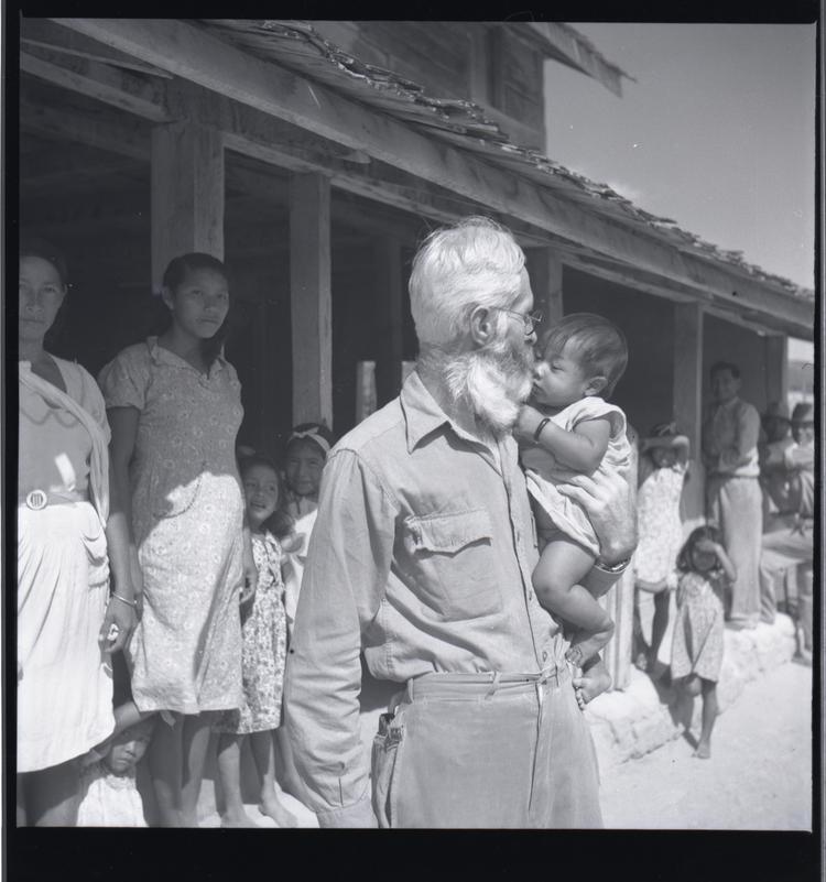 Black and white medium format negative of man in front of a building holding a baby (people behind in shade of building)
