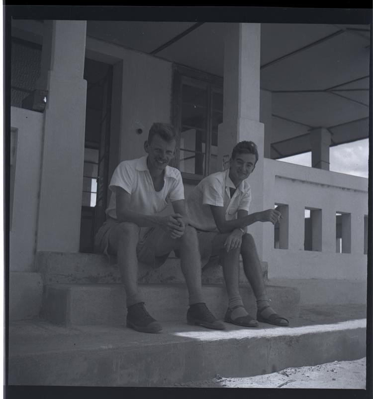 Image of Black and white medium format negative of 2 men in shorts sitting on the steps of a building