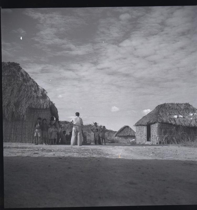 Image of Black and white medium format negative of man standing in front of group of villagers and their houses