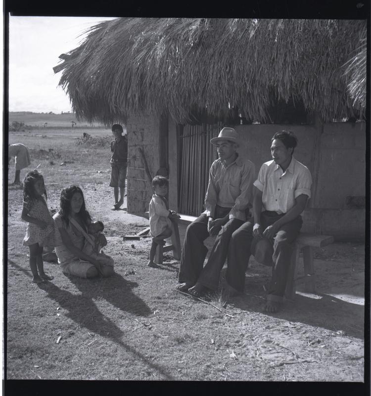 Black and white medium format negative of adults and children beside a hut