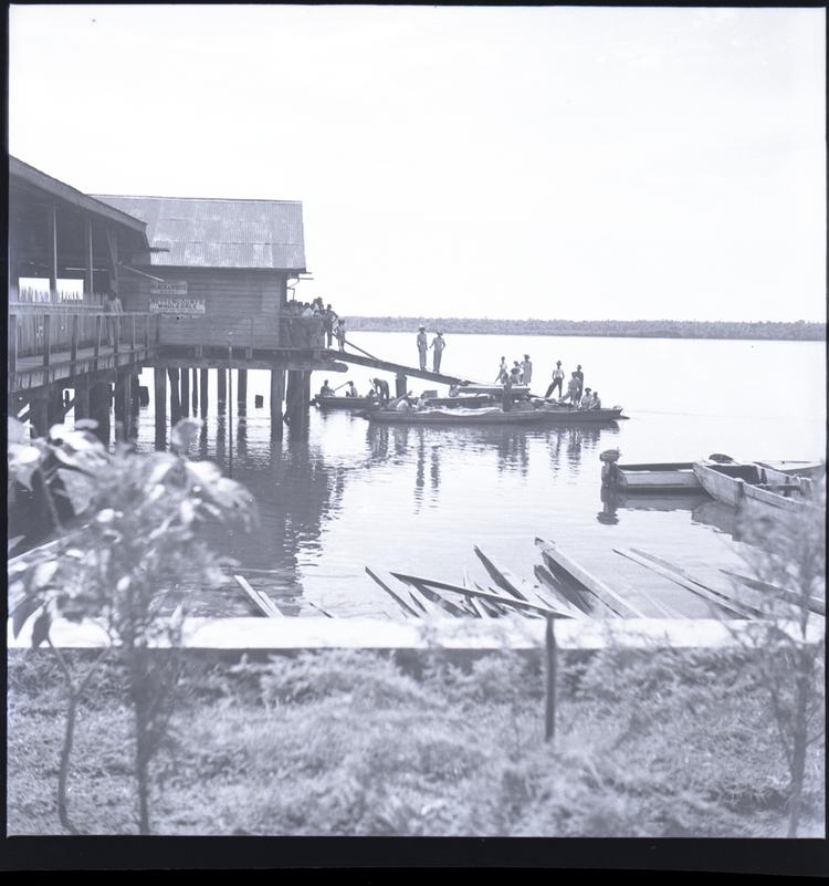 Black and white medium format negative of water's edge with boats and houses on stilts over the water